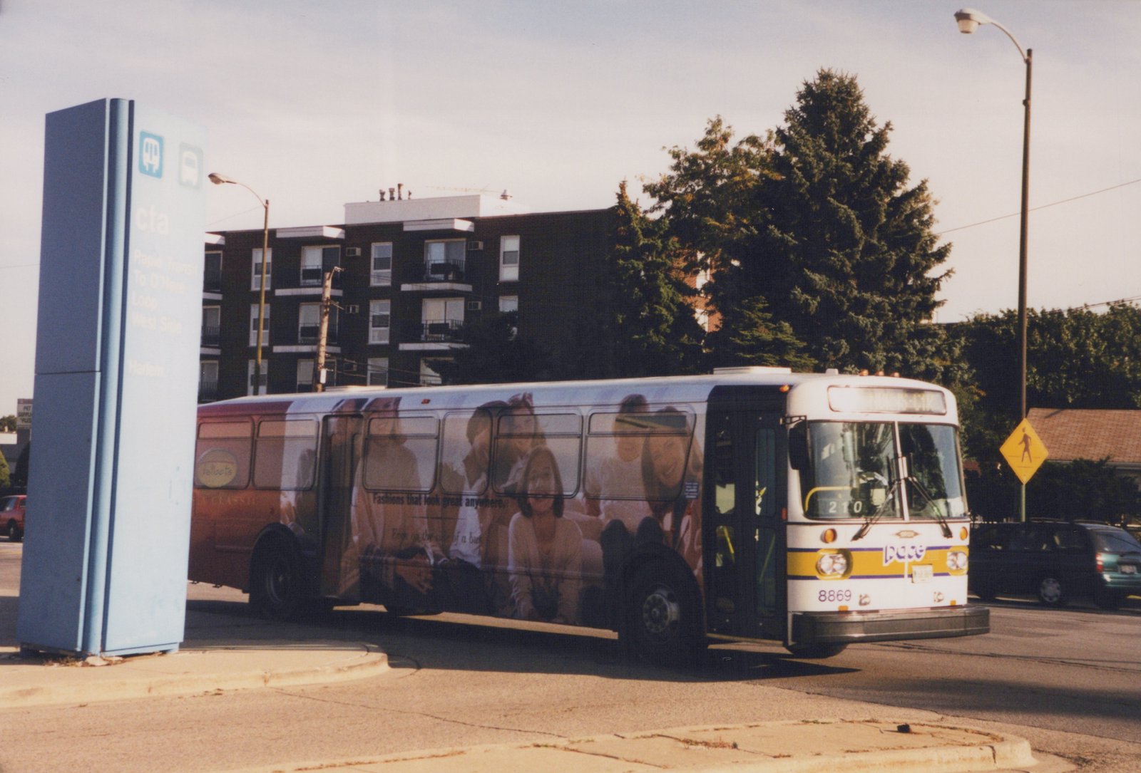 A white Pace bus with a yellow and purple stripe, number 8869, is shown from a three-quarter front view on a sunny street next to a CTA sign.