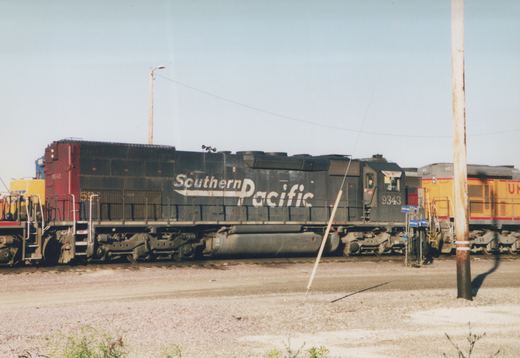 A black Southern Pacific locomotive with the number 9343 is parked next to a yellow Union Pacific locomotive with the number 602 in a gravel yard under a clear sky.