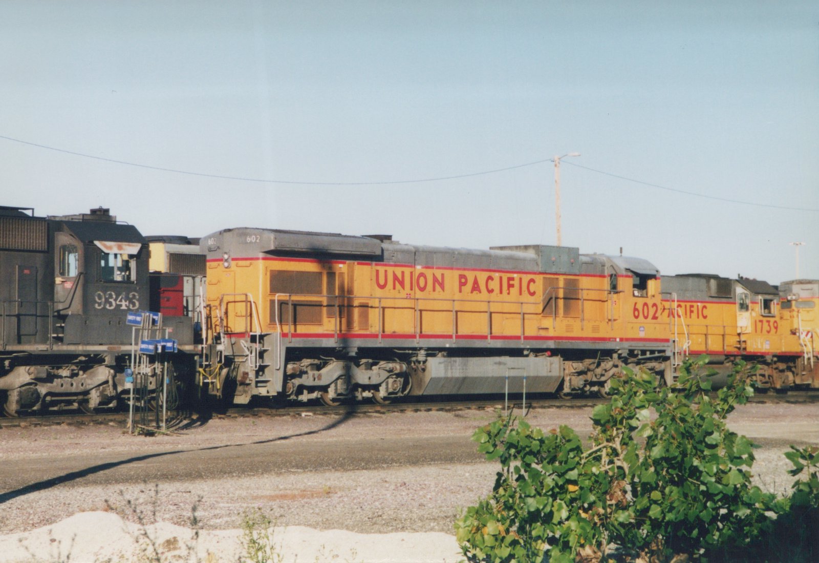 Three diesel locomotives in railroad yard, two in Union Pacific yellow livery and one in black Chicago and North Western livery.