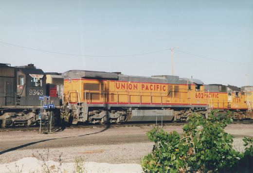 Three diesel locomotives in railroad yard, two in Union Pacific yellow livery and one in black Chicago and North Western livery.