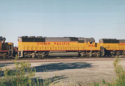 A yellow and red Union Pacific locomotive numbered 5954 with a trailing locomotive numbered 6282, standing on tracks in a rail yard under a clear sky.