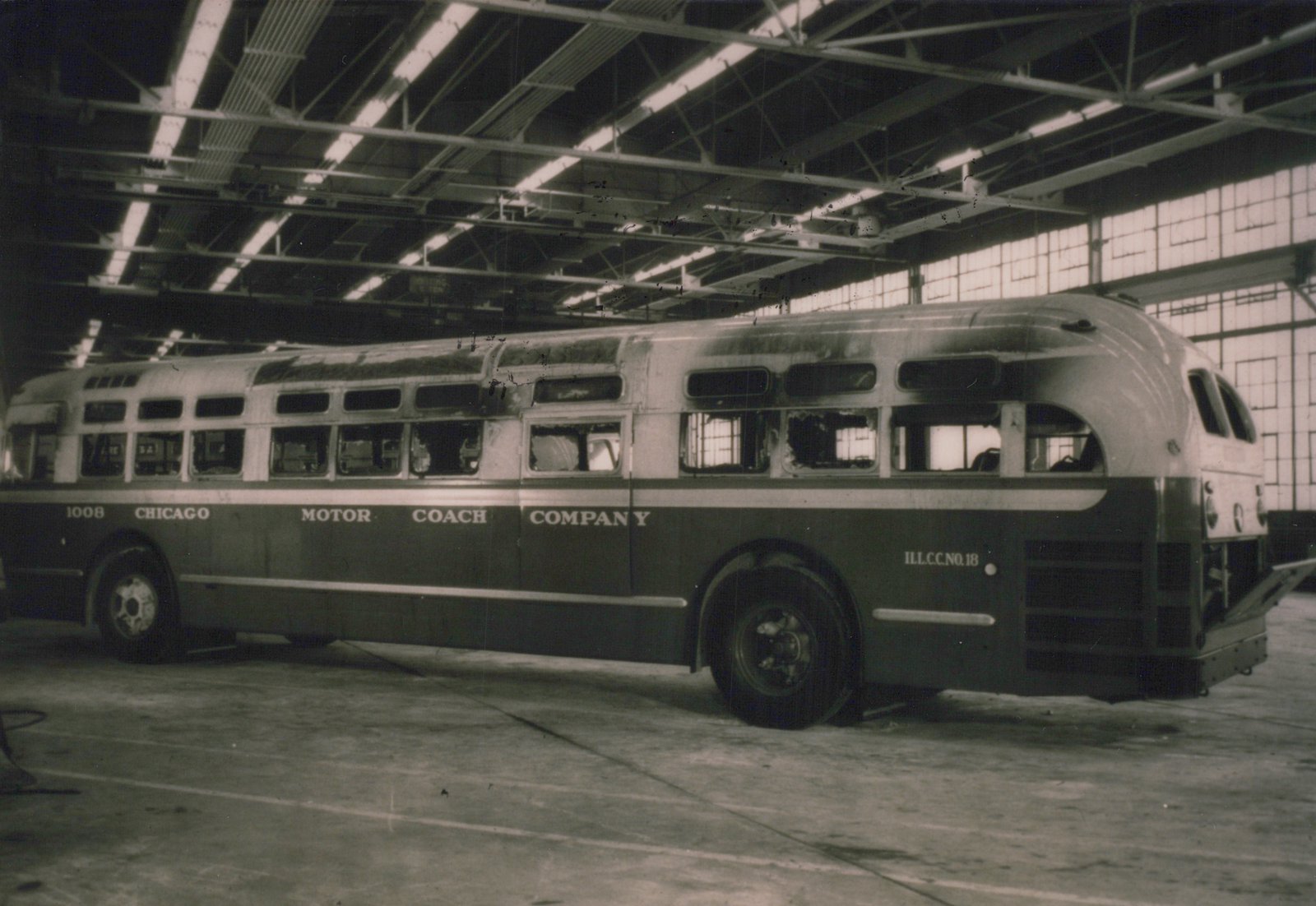 A side view of a vintage Chicago Motor Coach Company bus, number 1008, with a streamlined body, parked inside a large, well-lit bus garage.