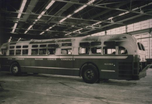 A side view of a vintage Chicago Motor Coach Company bus, number 1008, with a streamlined body, parked inside a large, well-lit bus garage.