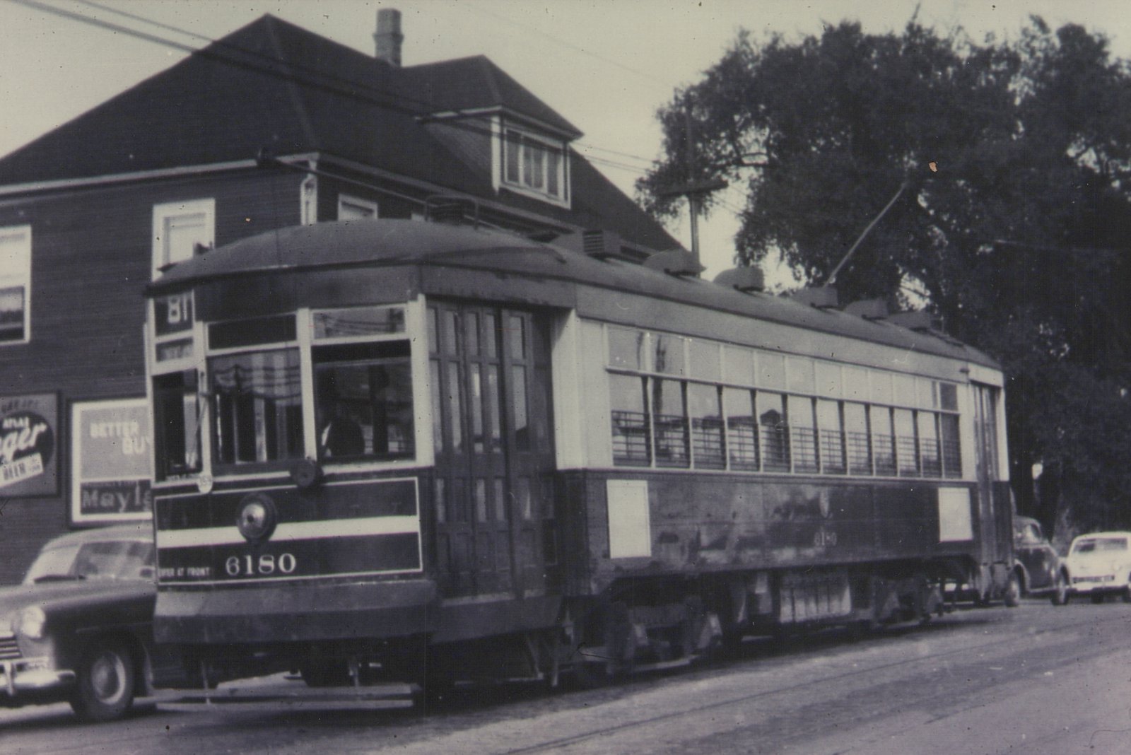 A black and white photo of a vintage Chicago Surface Lines streetcar numbered 6180 on a city street, with a 1950s sedan and a building in the background.