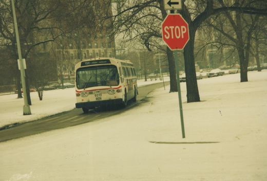 A white and red Chicago Transit Authority bus labeled 9212 and route 156 LaSalle/Jackson drives on a snowy street, with a red stop sign visible on the right and bare trees in the background.