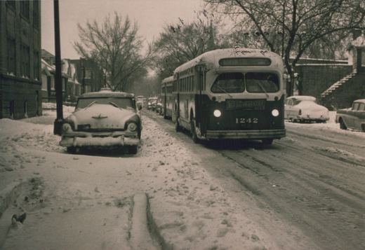 Black and white photo of a line of buses on a snow-covered city street, with one bus in the foreground showing the number 1242 and a Braumeister ad.